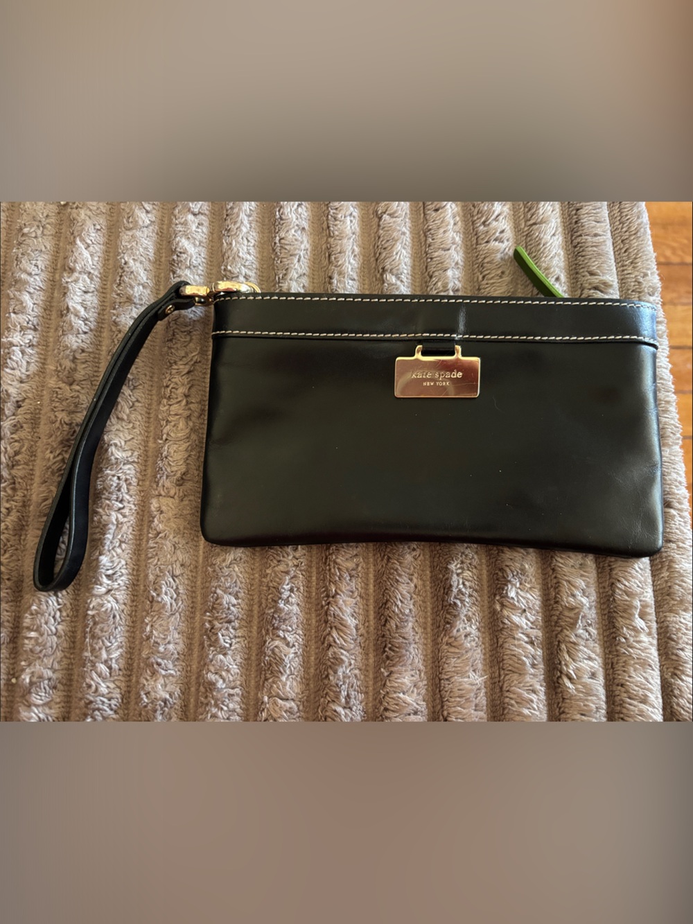 Kate Spade black leather wristlet with gold plaque and green polka dot inside .